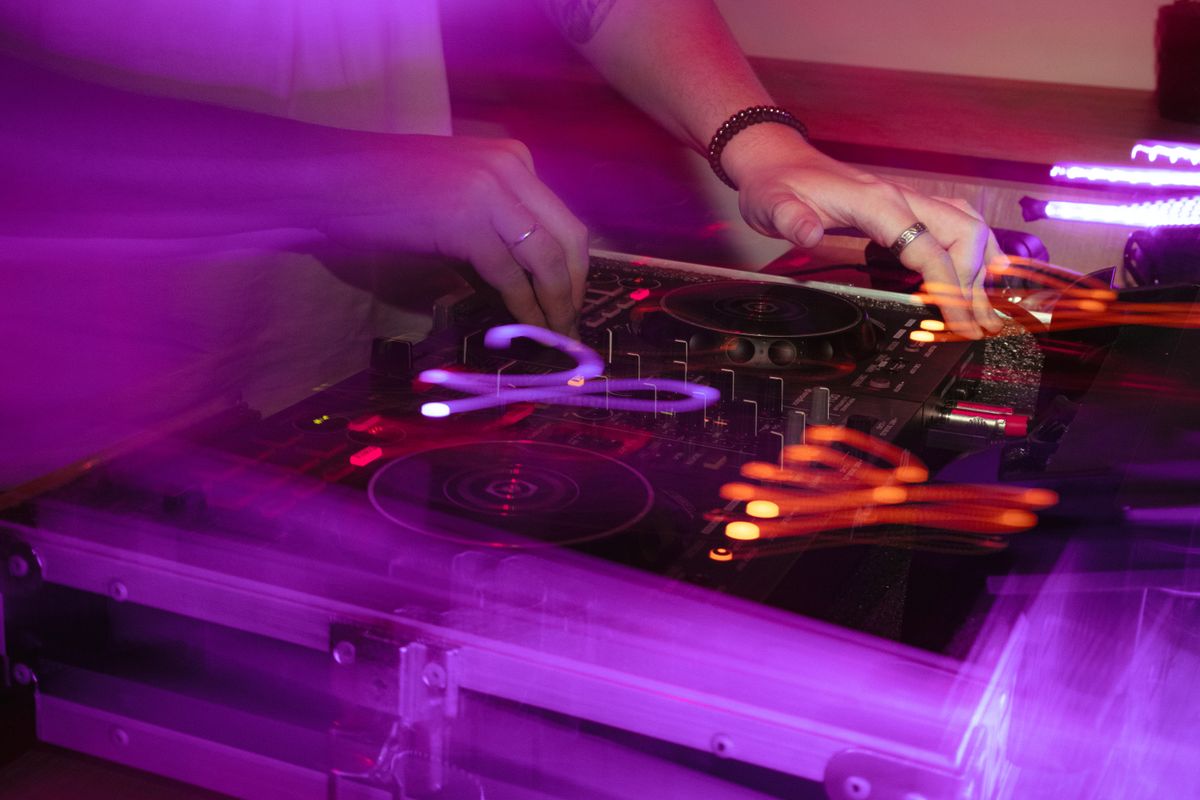 Hands at a DJ mixer under magenta light
